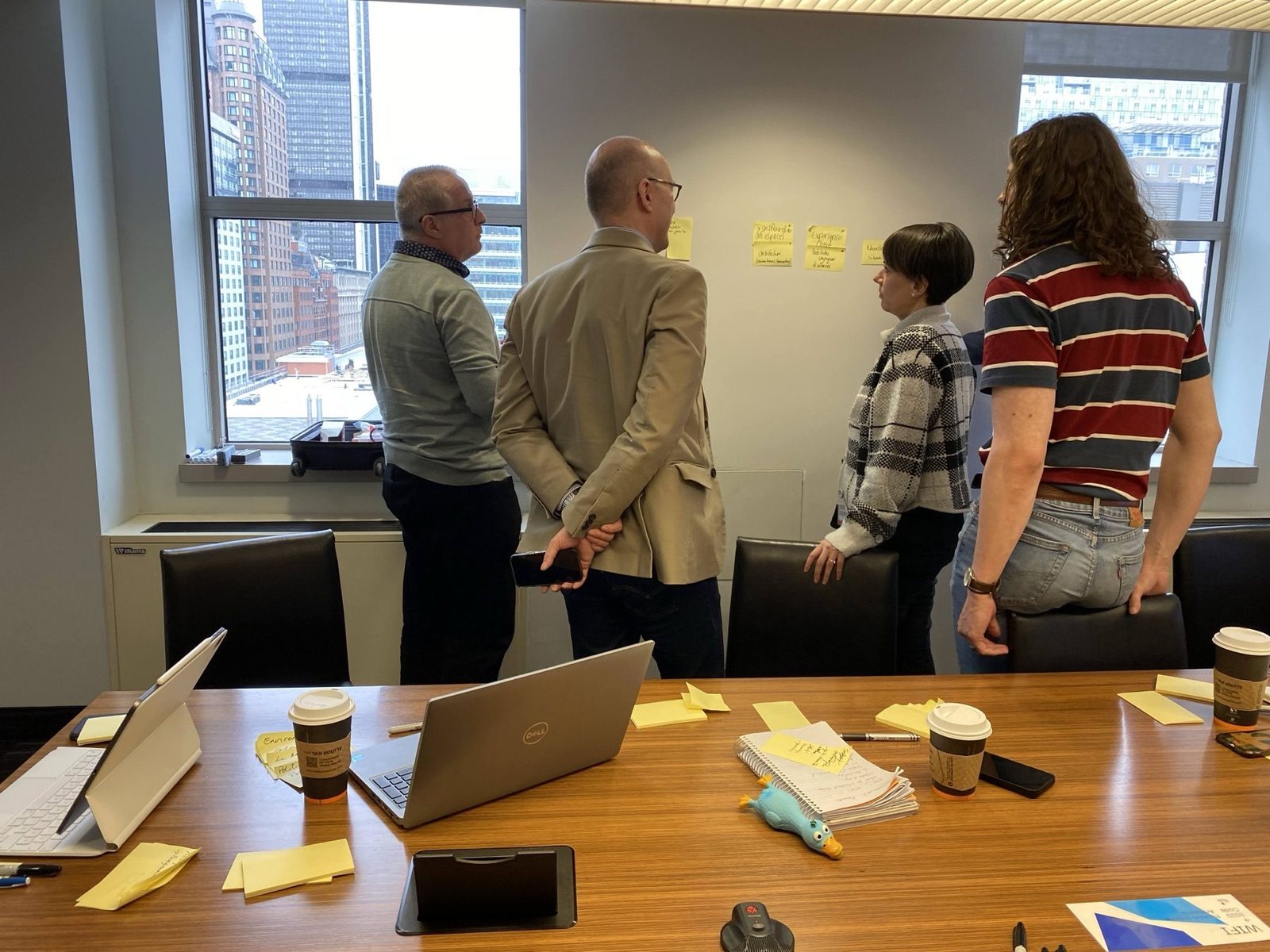 Quatre participants debout devant un mur de post-it, le centre-ville de Montréal par la fenêtre
