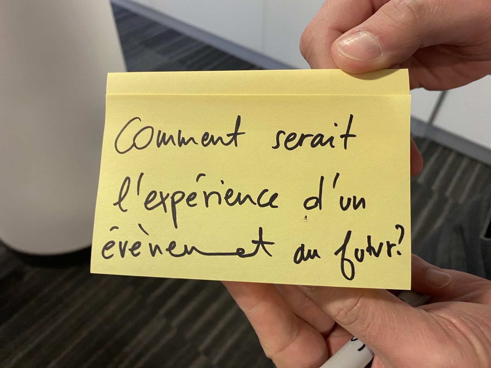 Une main tient un post-it : « Comment serait l’expérience d’un événement au futur ? »