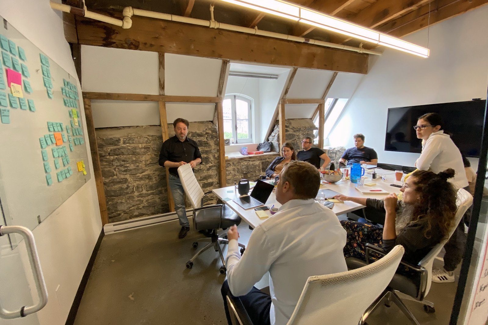 The sprint team around a long table in a loft office with wooden beams, sticky notes on the glass wall